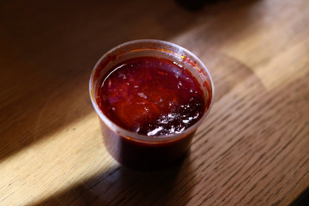A Delicious and Vibrant Red Sauce Delightfully Sitting in a Cup Resting on a Wooden Surfaceの写真素材