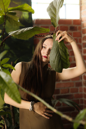 A woman poses elegantly with a large leaf in a lush indoor greenery, blending art and natureの写真素材