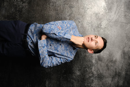 A Thoughtful Young Man in a Stylish Blue Shirt Posing Elegantly Against a Dark Background