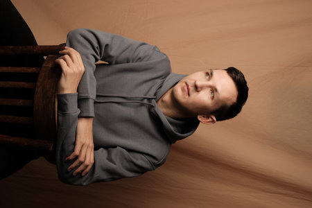 A Contemplative Young Man Dressed in a Casual Hoodie Sitting Comfortably on a Chairの写真素材