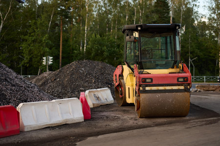 A Heavy Roller is operating on a Construction Site that is located near a large pile of Gravel