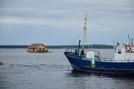 A charming fishing boat is gently floating near a beautiful house situated in the calm watersの写真素材