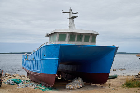 An Abandoned Blue Fishing Boat Resting on the Serene Shoreline, Evoking a Sense of Nostalgiaの写真素材