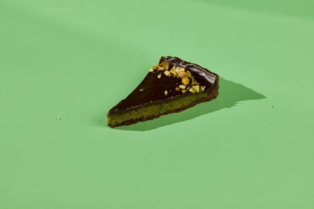A delicious and visually appealing slice of Chocolate Pistachio Tart placed on a green backgroundの写真素材