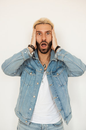 A surprised young man with blond hair in a stylish denim jacket shows a cheerful attitude