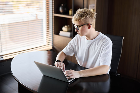 A Young Professional Engaged in Work While Using a Laptop at a Modern Stylish Deskの写真素材