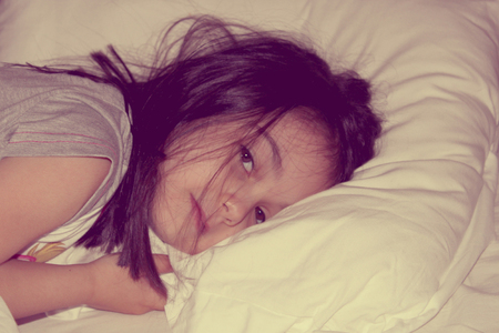 Vintage photo of little girl tucked into bedの写真素材