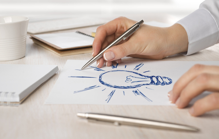 Business woman hand drawing on paper a light bulbの写真素材