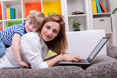 Woman with child lie on sofa and using computerの写真素材