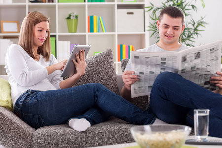 Woman with tablet and husband with newspaper reading newsの写真素材