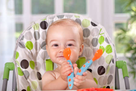 Smiling baby eating with spoon and forkの写真素材
