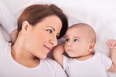 Young mother with her baby relaxing on bedの写真素材