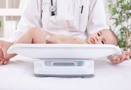Female pediatrician weighing adorable baby in officeの写真素材