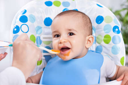 Smiling happy baby child eating with spoonの写真素材
