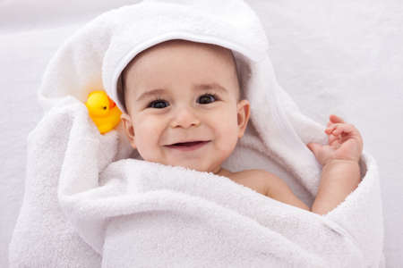 Adorable baby smiling wrapped in white towel with yellow duck, isolated on whiteの写真素材