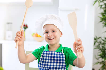 Young beautiful child with chef cap smiling and holding scoops in the kitchenの写真素材