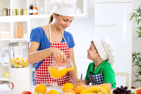 Beautiful happy mother pour orange juice to her child boy in kitchenの写真素材