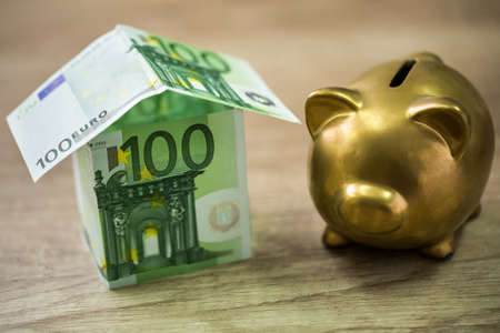 Piggy bank and house built of 100 euro banknotes, savings conceptの写真素材