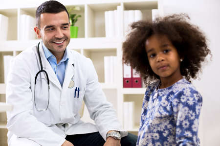 Pediatrician looking and smiling to his little girl patientの写真素材