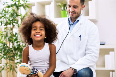 Doctor pediatrician examining cute smiling african girl with stethoscopeの写真素材