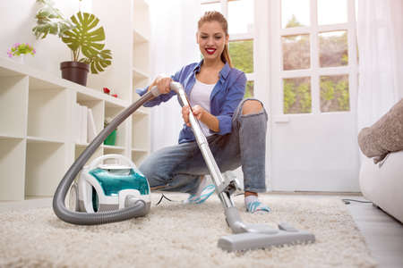 Beautiful young woman cleaning with vacuum cleaner at homeの写真素材