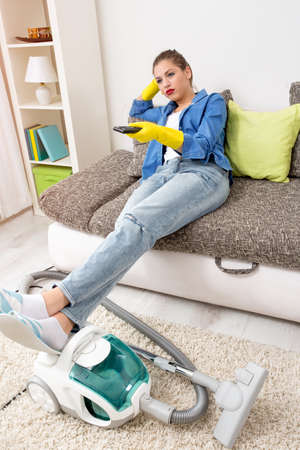 Tired woman watching television at home after vacuumingの写真素材