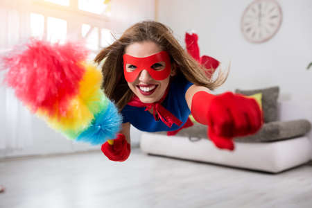 Woman superhero flying through the room with  a feather dusterの写真素材