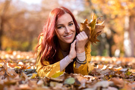 Smiling girl lying in autumn park and holding leavesの写真素材