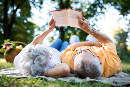 Lovely senior couple resting at park, reading a bookの写真素材