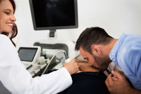 Happy couple at gynecologist clinic, happy father kissing wifes bellyの写真素材