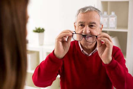 Senior man patient takes glasses aftere change of diopter, at clinic
