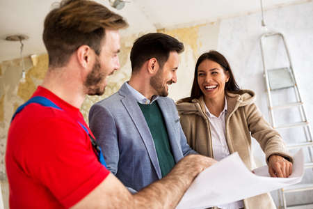 Builder handyman shows to young couple details blueprints of their homeの写真素材