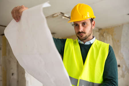 Young architect checking blueprint of building reconstruction, at construction siteの写真素材