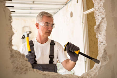Worthy senior man working with hammer and tool while demolish wallの写真素材