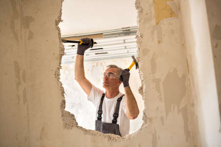 Senior worker using tool at contruction site, demolish wall