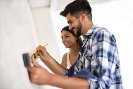 Smiling young couple measuring wall with level tool