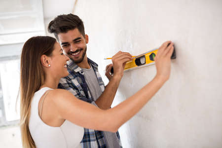Smiling young couple measuring wall with level toolの写真素材