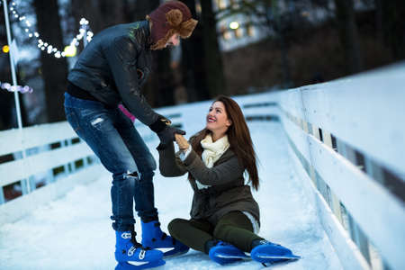 Man helping attractive woman to rise up on skating rinkの写真素材