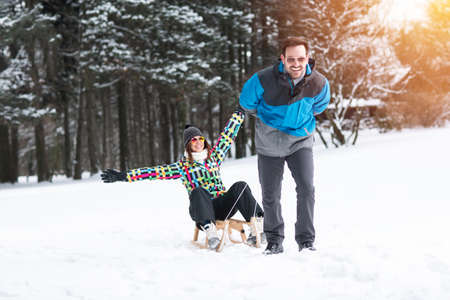 Young happy couple having fun in winter nature with sleighの写真素材