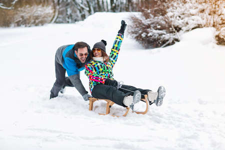 Smiling happy couple having fun on winter day and using sleigh