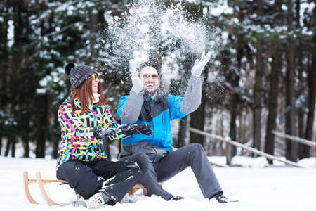 Lovely couple sitting on sleigh and playing with snow, winter conceptの写真素材