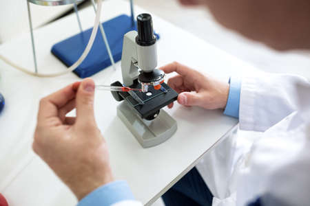 Close up scientist hands with microscope, blood test analyzing