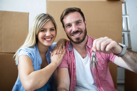 Young couple celebrating moving to new home sitting among boxesの写真素材