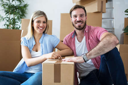Young happy attractive couple celebrating moving to new home sitting among boxes