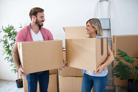 Smiling young couple holding boxes and packing for moving at new house