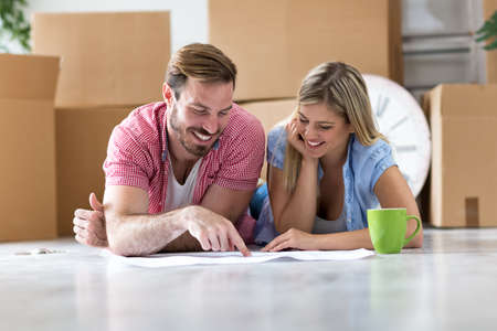 Young couple moving in new house, unpacking things and looking at plan of therenew home