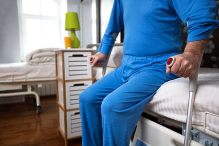Senior immobility man stand up from bed with the help of crutches, close upの写真素材