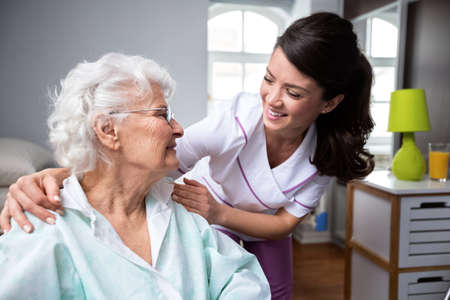 Smiling nurse and old woman patient at wheelchair at private nursing homeの写真素材