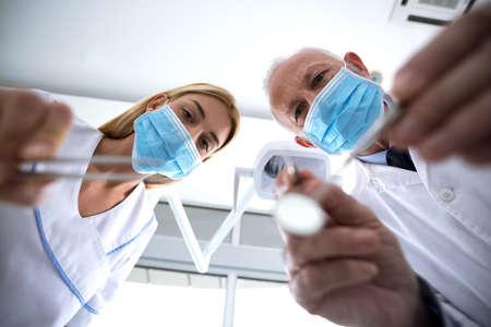 Dentist and assistant with sterile mask and dental instruments held examine teeth of patient in dental clinicの写真素材