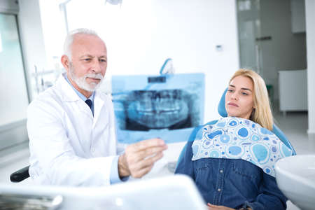 Dentist and patient are considering necessary treatments of teeth looking at X-ray image